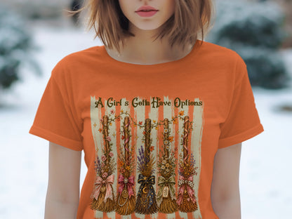 Orange t-shirt with five decorated brooms and the text "A Girl's Gotta Have Options".