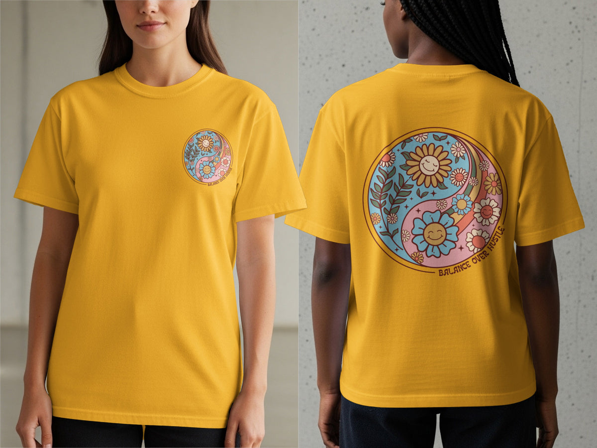 Yellow t-shirt with a yin-yang design featuring smiling flowers and the text "BALANCE OVER HUSTLE".