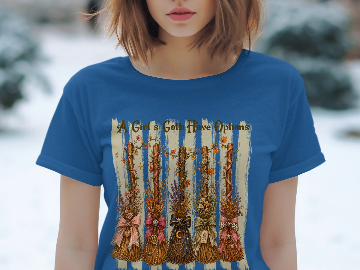 Blue t-shirt with a graphic of five decorated brooms and text that reads "A Girl's Gotta Have Options."