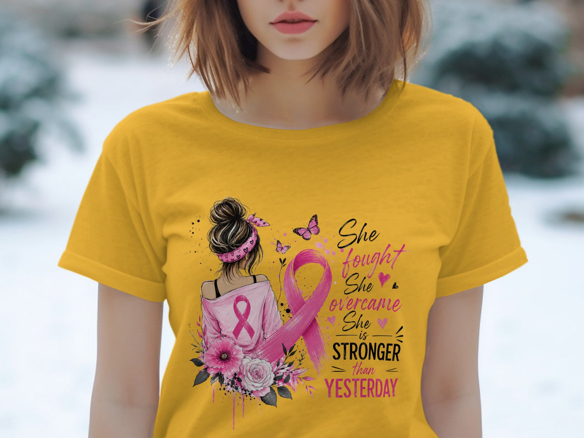 Yellow t-shirt with graphic of woman, pink ribbon, flowers, butterflies, and text "She fought, she overcame, she is stronger than yesterday".
