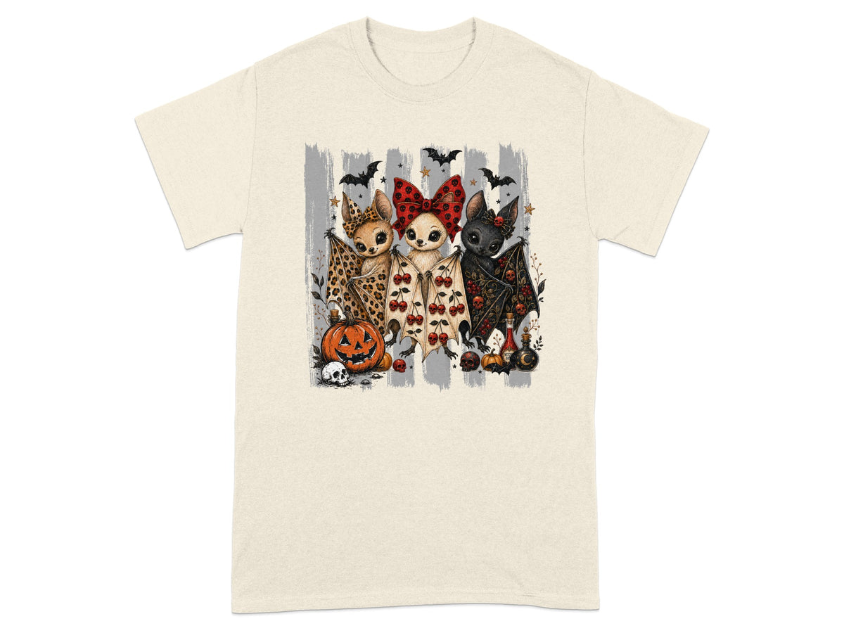 Three cartoon bats with Halloween-themed outfits and decorations on a cream t-shirt.