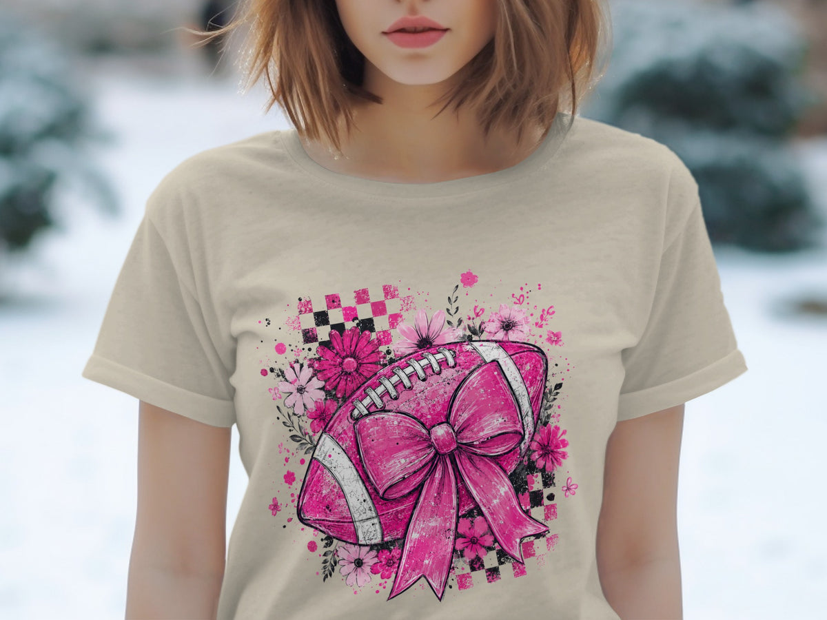 Pink football with bow and flowers graphic on a cream t-shirt.