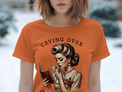Orange t-shirt with text "CRYING OVER" and illustration of a crying woman reading a book.