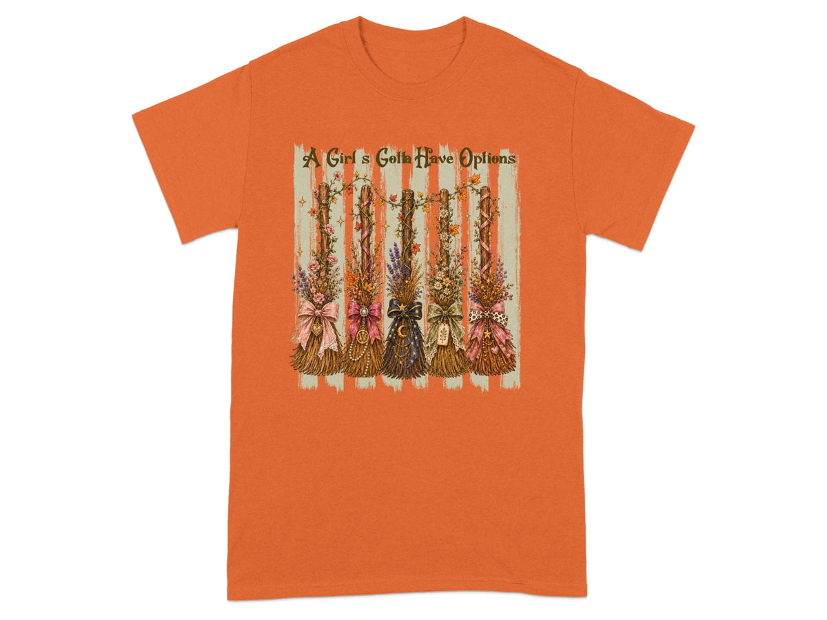 Orange t-shirt with graphic of five decorated broomsticks and text "A Girl's Gotta Have Options".