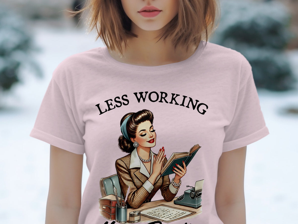 Pink t-shirt with "LESS WORKING" text and retro illustration of a woman reading.