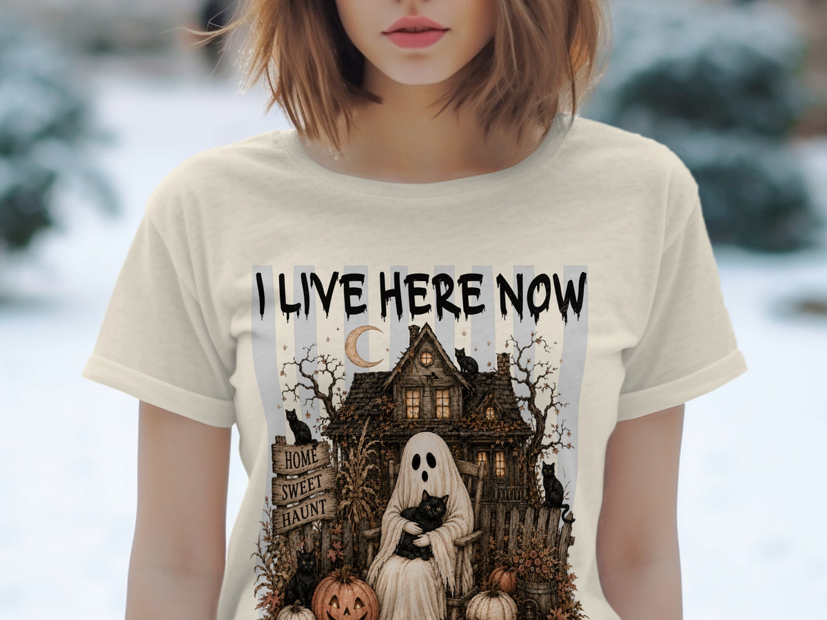T-shirt with "I Live Here Now" text, a ghost holding a cat, haunted house, and pumpkins.