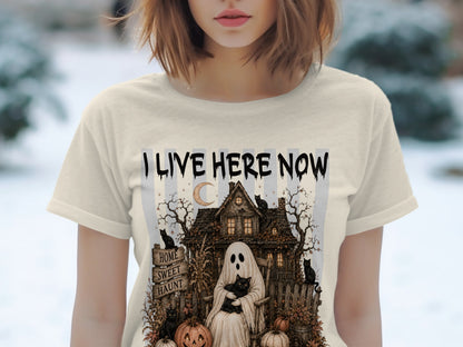 T-shirt with "I Live Here Now" text, a ghost holding a cat, haunted house, and pumpkins.