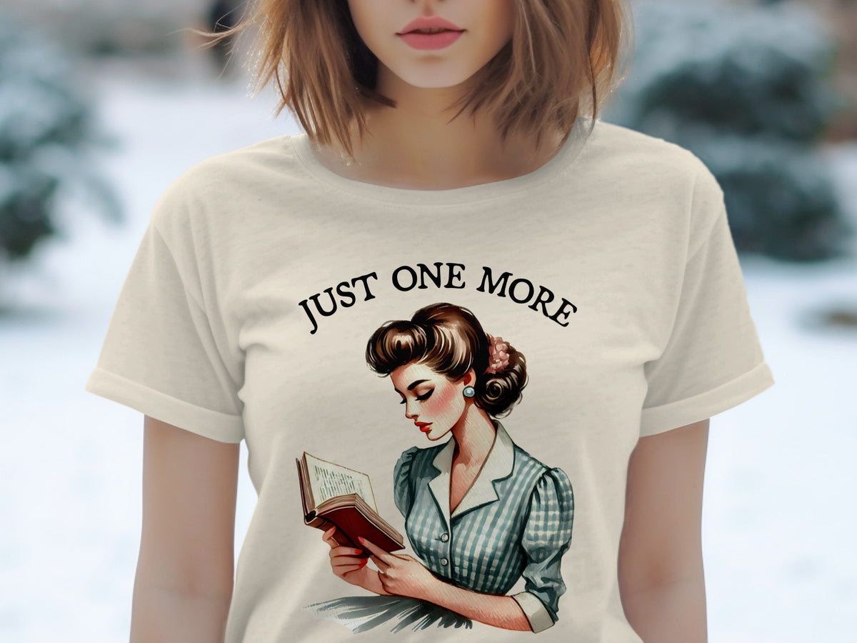 Light beige t-shirt with "JUST ONE MORE" text above a retro drawing of a woman reading.