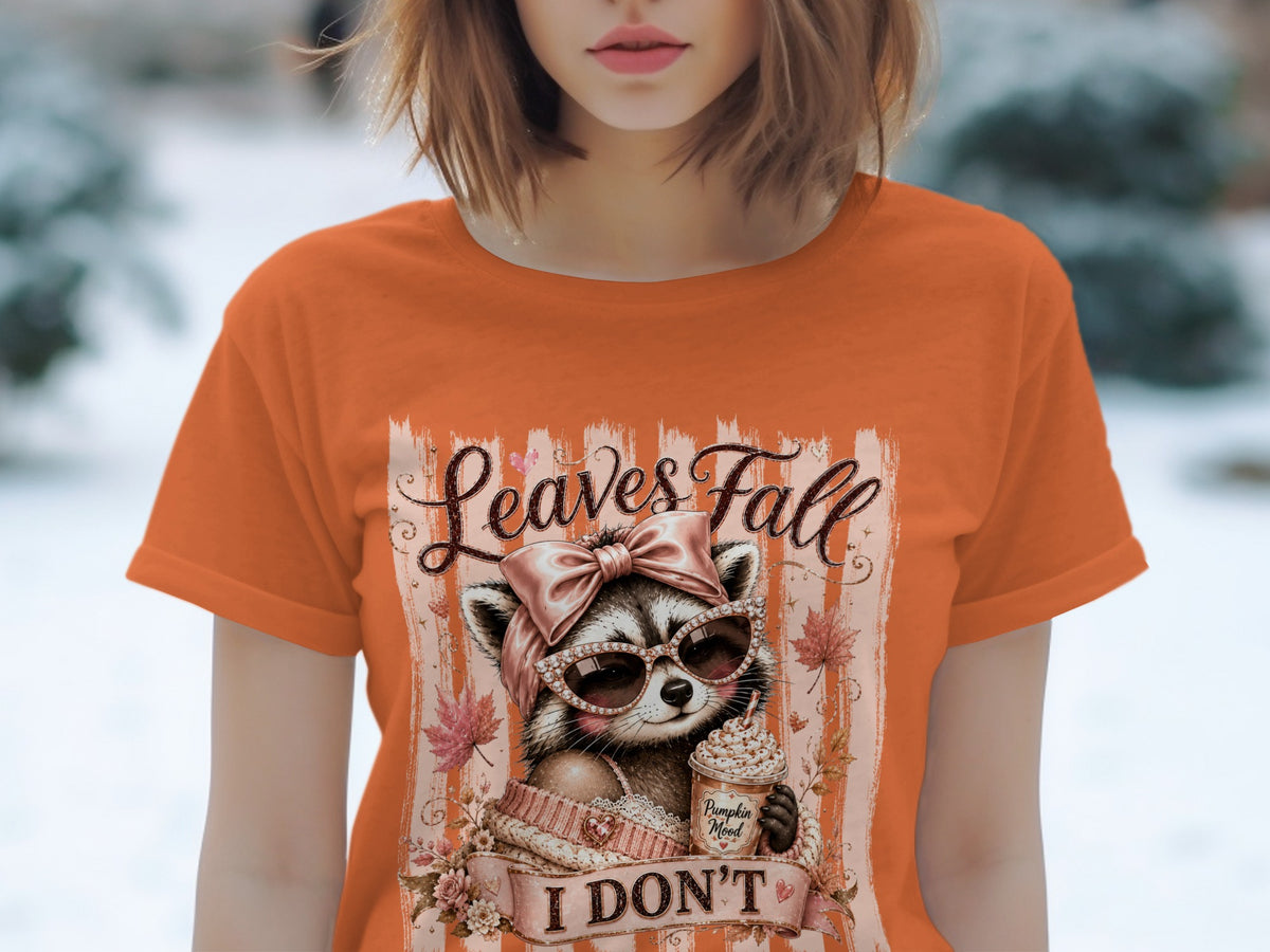 Orange t-shirt with graphic of raccoon in sunglasses, holding a pumpkin spice latte, with text "Leaves Fall I DON'T".