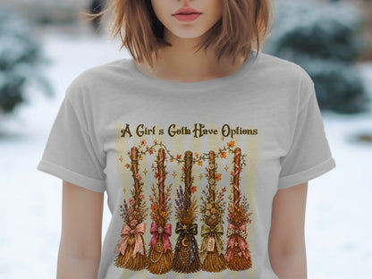 T-shirt with decorative brooms and "A Girl's Gotta Have Options" text.