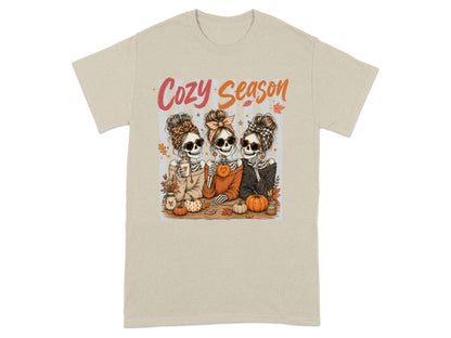 Three skeletons with Halloween accessories, holding drinks, text reads "Cozy Season."