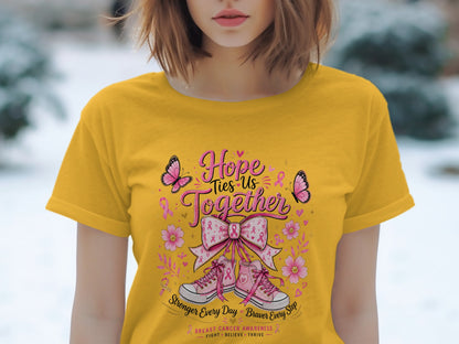 Yellow t-shirt with pink breast cancer awareness graphic of butterflies, ribbons, flowers, sneakers, and inspirational text.