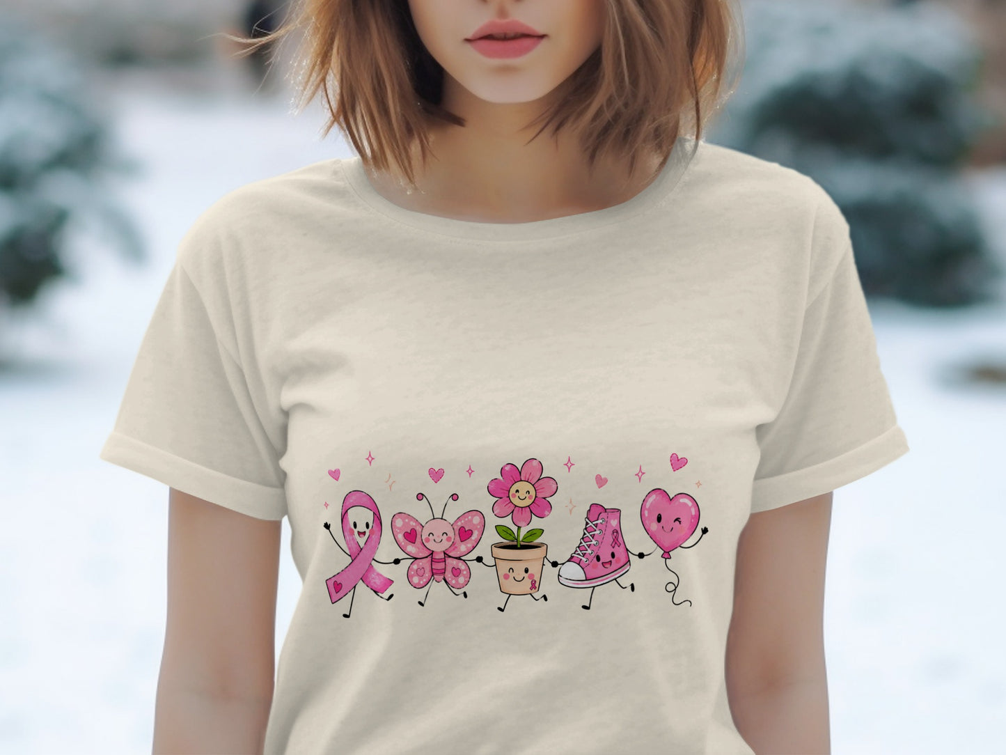 Cream t-shirt with cartoon breast cancer ribbon, butterfly, flower, shoe, and balloon characters.