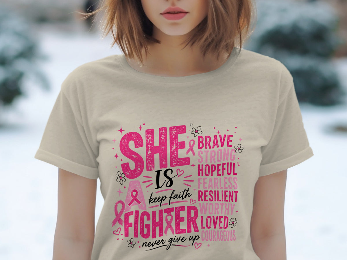 Cream t-shirt with pink text: SHE IS A FIGHTER, KEEP FAITH, NEVER GIVE UP, BRAVE, STRONG, HOPEFUL, FEARLESS, RESILIENT, WORTHY, LOVED, COURAGEOUS.