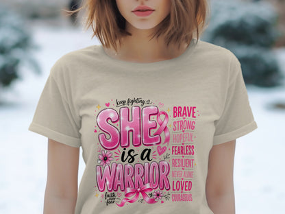 "She is a warrior" text with supportive words and breast cancer ribbon on a beige t-shirt.