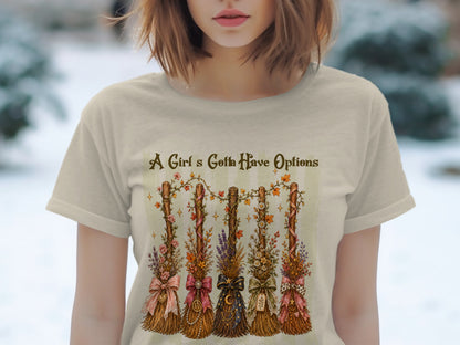 Cream t-shirt with five decorated brooms and text "A Girl's Gotta Have Options".