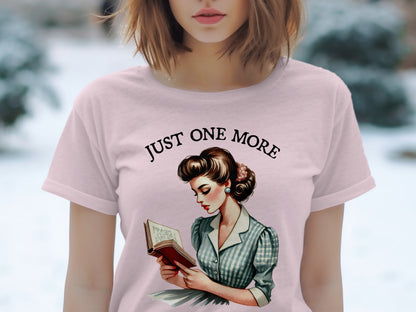 Pink t-shirt with illustration of a woman reading and text "JUST ONE MORE".