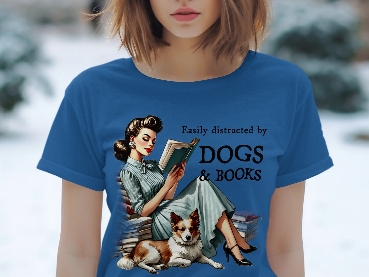 Blue t-shirt with graphic: Woman reading surrounded by books with dog, text "Easily distracted by DOGS & BOOKS".