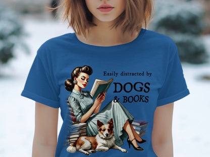 Blue t-shirt with graphic: Woman reading surrounded by books with dog, text "Easily distracted by DOGS & BOOKS".