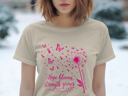 Light tan t-shirt with pink dandelion, butterflies, ribbons, and text "Hope blooms, strength grows."