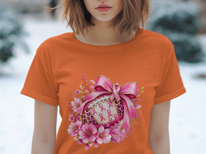 Orange t-shirt featuring a football adorned with pink ribbons, bow, leopard print, and flowers.