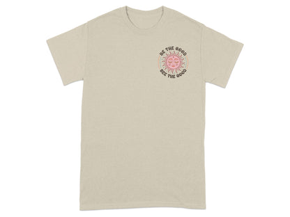 Beige t-shirt with a pink sun graphic and text "Be the good, See the good".