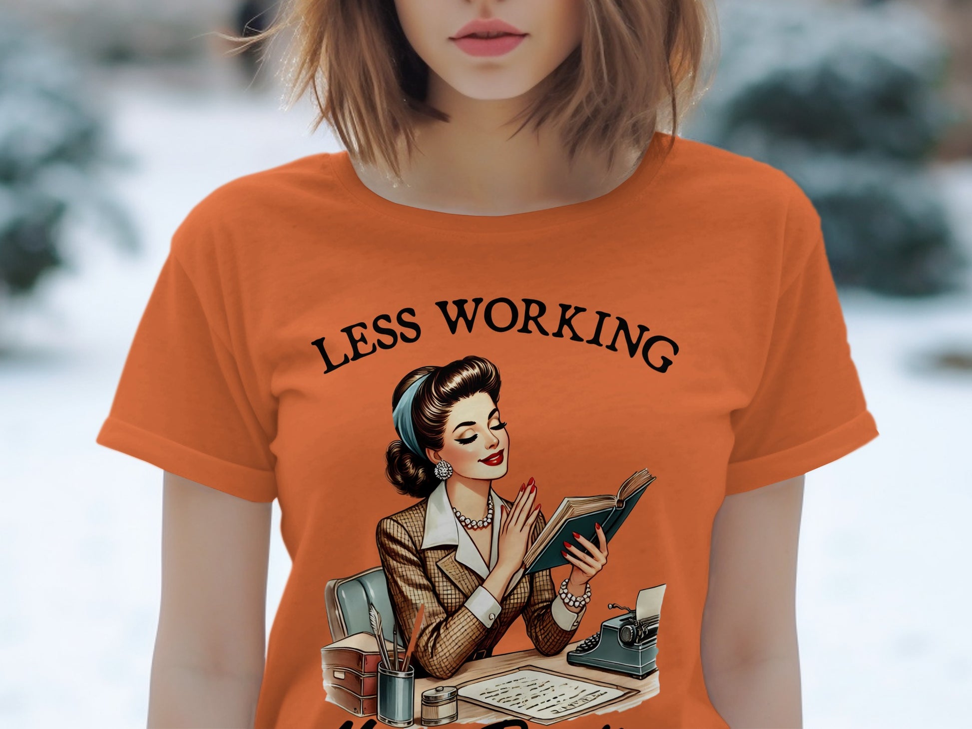 Orange t-shirt with "LESS WORKING" text and vintage illustration of woman reading.
