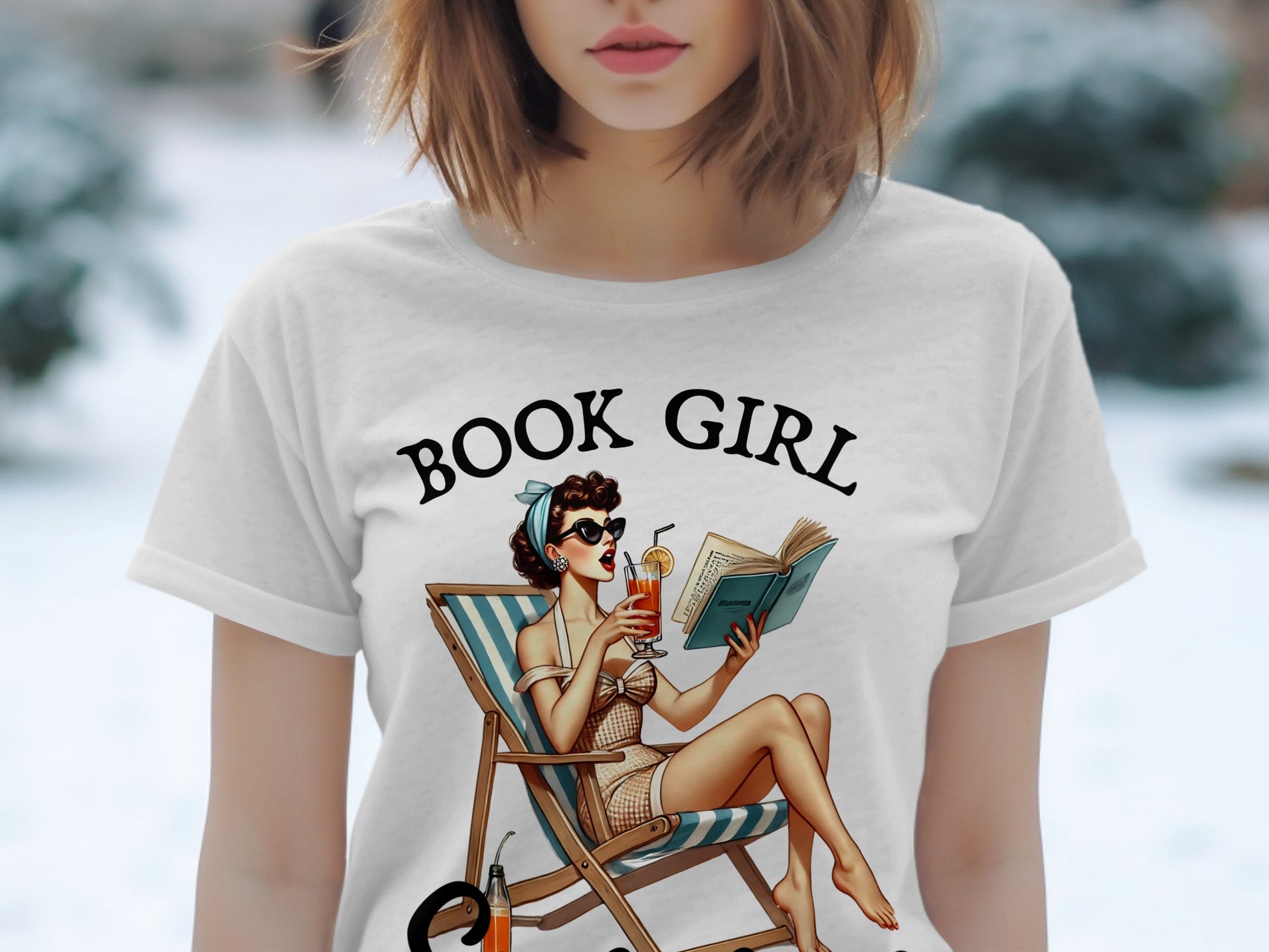 White t-shirt with "BOOK GIRL" text and illustration of woman reading in deck chair.