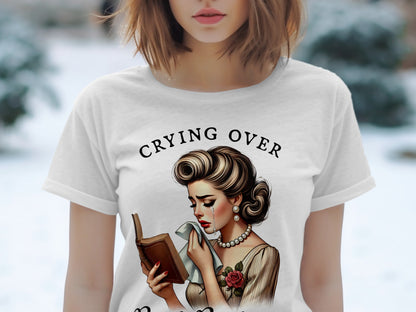 Woman crying over a book with text "Crying Over" on a white t-shirt.