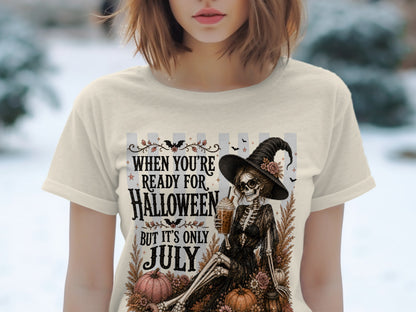 Skeleton witch with drink graphic on cream t-shirt, reads "When You're Ready For Halloween But It's Only July".