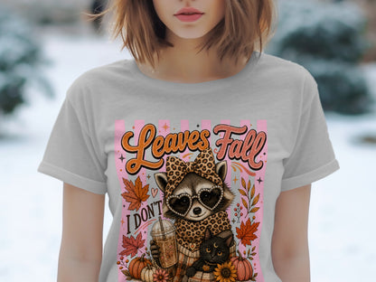 Raccoon in leopard print holding a coffee, with cat and pumpkins, says "Leaves Fall".