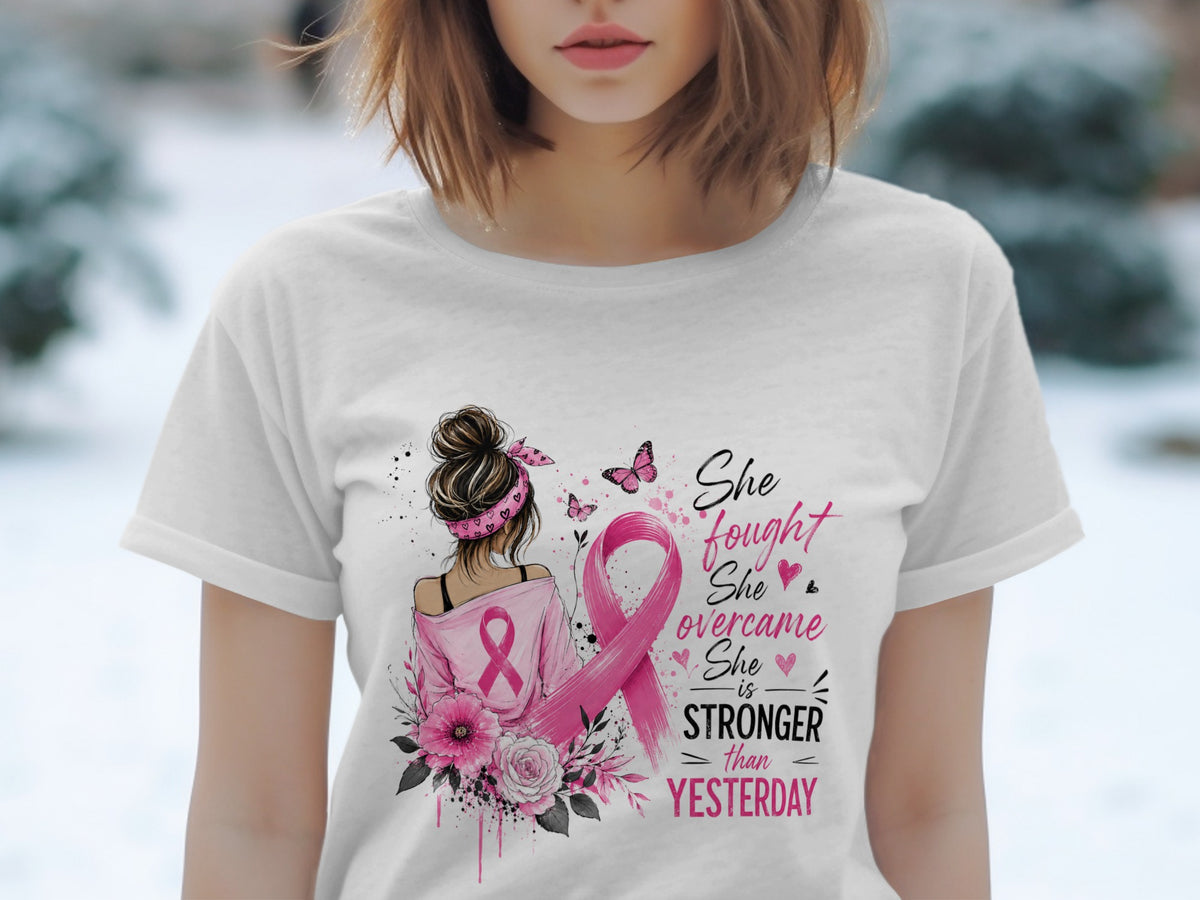White t-shirt with breast cancer ribbon and inspirational text: "She fought, she overcame, she is stronger than yesterday."