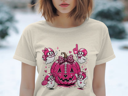 Pink football-themed jack-o'-lantern with football-playing ghosts and hearts on a cream t-shirt.