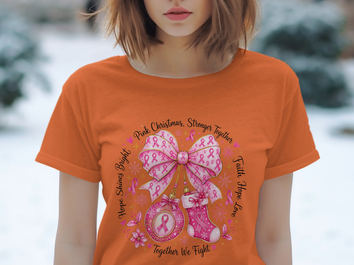 Orange t-shirt with a circular design featuring pink ribbons, a bow, ornament, stocking, and text.