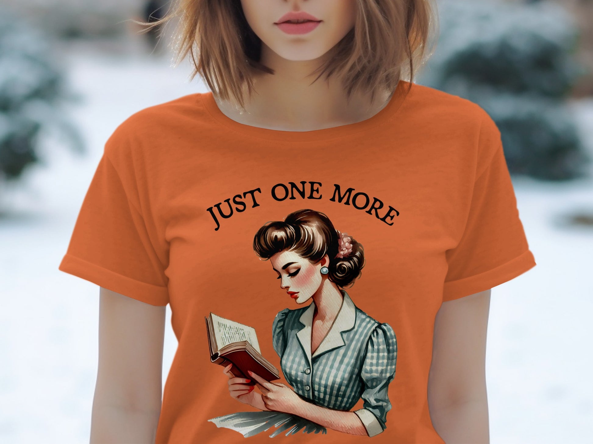 Orange t-shirt with "JUST ONE MORE" and a retro illustration of a woman reading.