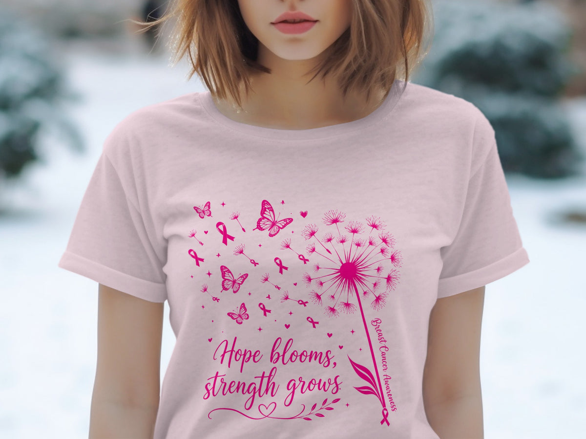 Pink t-shirt with a dandelion, butterflies, and pink ribbons, text says "Hope blooms, strength grows."