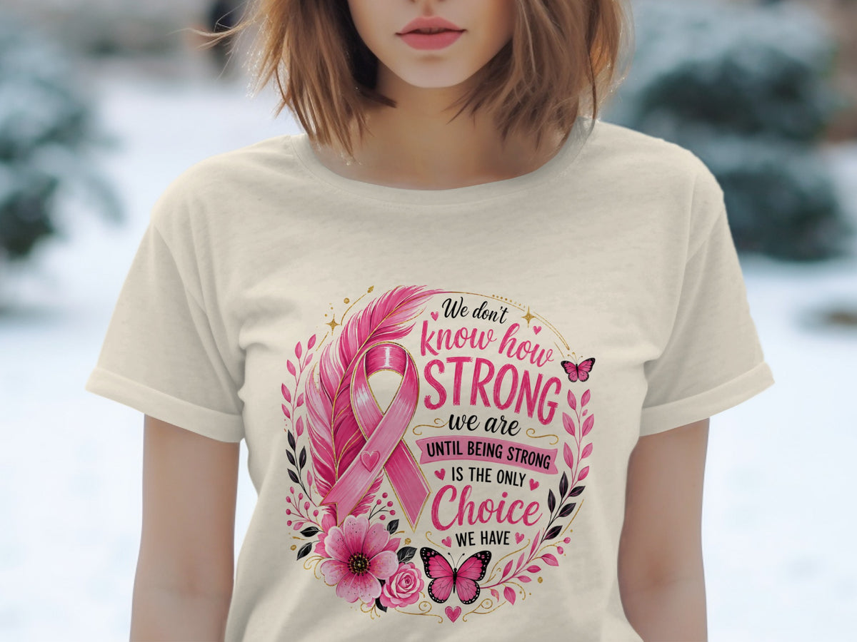 Light-colored t-shirt with a pink ribbon design and text "We don't know how strong we are until being strong is the only choice we have".